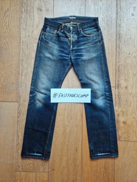 Example verification photo: a pair of faded raw denim jeans laid flat on a wooden floor, with a card reading #FASTFADESCOMP written by hand lying on the legs.